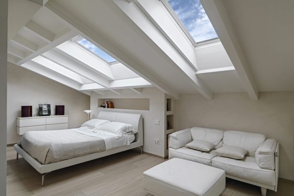 interior shot of a bedroom in the modern attic-room in the foreground the leather sofas with footrest in the background there is the bed illuminated by two skylights
